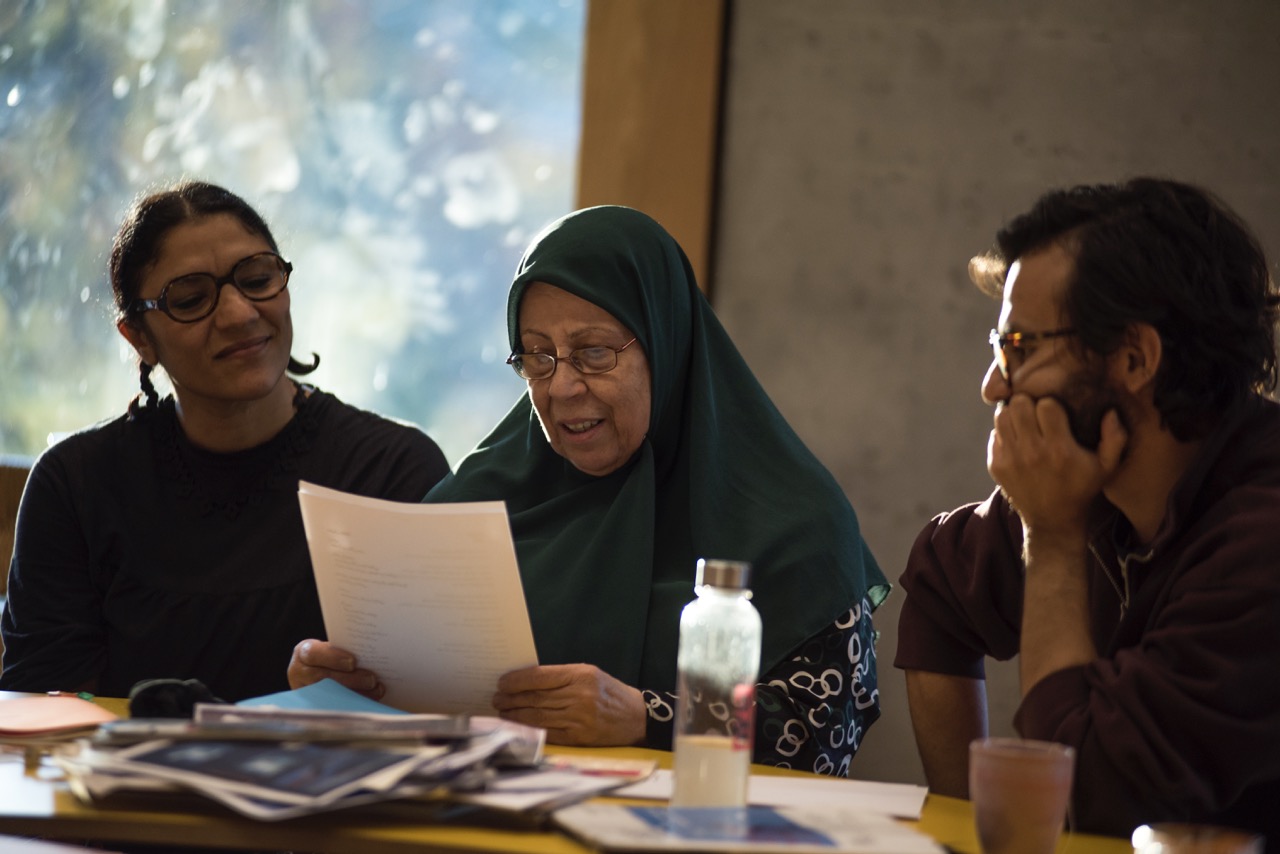 Drei Menschen sitzen am Tisch, einer liest vor.