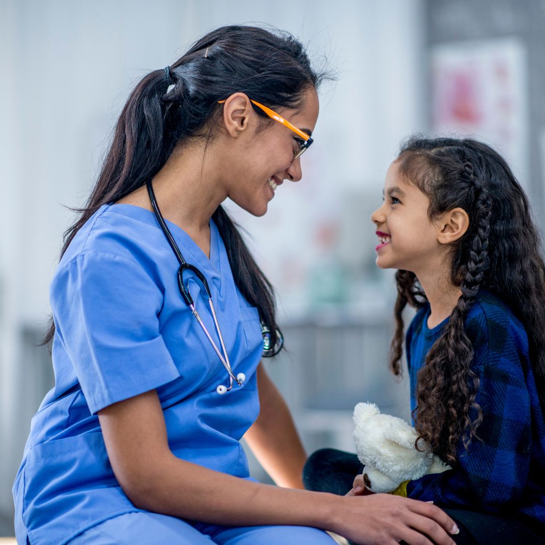 Eine Ärztin und ein kleines Mädchen sitzen fröhlich nebeneinander.