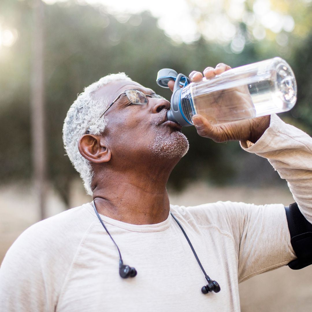 Ein älterer Mann trink Wasser aus einer Flasche. 
