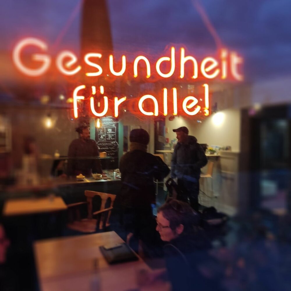 Durch das Fenster kann man das Innere einer Cafeteria sehen, in der sich Menschen aufhalten.